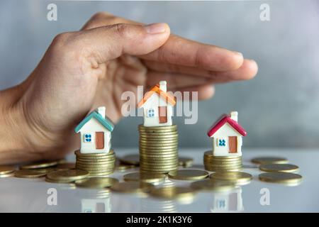 Frau Hand Schutz auf Stapel Münzen und Haus Modell auf dem Tisch.Konzept der Immobilien-Management. Investments und Risikomanagement. Stockfoto
