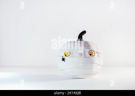 Lustige und niedliche Kürbis-Mumie mit Spinne auf dem weißen Hintergrund. Weißer Kürbis mit beängstigtem und besorgtem Look. Angst vor Insekten. Halloween-Dekor und BA Stockfoto