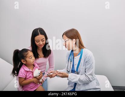 Japanischer Elternteil mit weiblichem Kind während der medizinischen Untersuchung im Krankenhaus. Kinderarztberatung Stockfoto