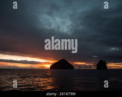 Sonnenuntergang über dem Atlantik von den portugiesischen Azoren. Eine abgehackte Küstenlinie während des Sonnenuntergangs mit felsigen Aufschlüssen und einem erstaunlichen Sonnenuntergang. Stockfoto