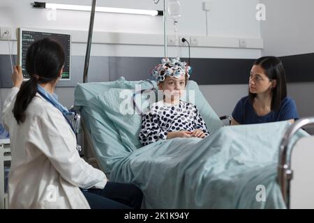 Der Kinderarzt überwacht den Gehirnzustand eines hospitalisierten Mädchens mithilfe eines EEG-Headsets. Neurologist, der die Entwicklung neurologischer Krankheiten bei kranken Kindern in einer Einrichtung für die pädiatrische Gesundheitsversorgung misst. Stockfoto