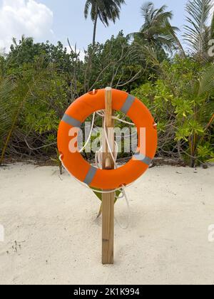 Eine leuchtend orangefarbene Rettungsboje, die für den Notfall auf einer Insel auf den Malediven am Strand platziert wird. Stockfoto