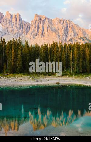 Atemberaubende Aussicht auf den Karersee (Lago di Carezza) mit seinem smaragdgrünen Wasser, wunderschönen Bäumen und Bergen in der Ferne an einem sonnigen Tag Stockfoto