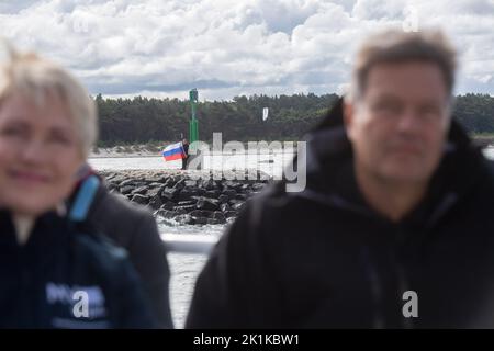 Deutschland. 19. September 2022. Lubmin, Deutschland. 19. September 2022. Ein Demonstrator schwenkt russische Flaggen am Hafeneingang von Lubmin im Vordergrund Robert Habeck (Bündnis 90/die Grünen), Bundesminister für Wirtschaft und Klimaschutz, und Manuela Schwesig (SPD), Ministerpräsidentin von Mecklenburg-Vorpommern, sitzen auf einem Schiff und besichtigen das Energiegebiet Lubmin. Quelle: Stefan Sauer/dpa/Alamy Live News Quelle: dpa picture Alliance/Alamy Live News Stockfoto