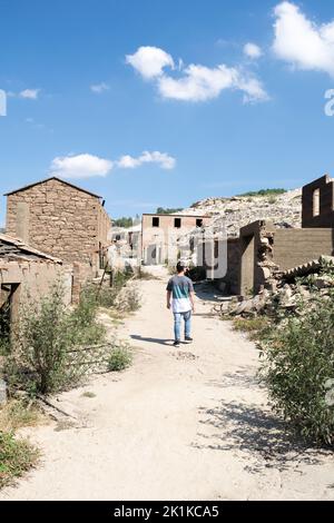 Rückansicht eines Mannes, der an verlassenen Häusern in der Geisterstadt Aceredo am Stausee Alto Lindoso, Lobios, Ourense, Galicien, Spanien, vorbeigeht Stockfoto