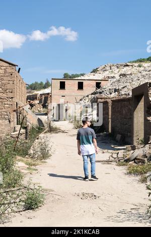 Rückansicht eines Mannes, der an verlassenen Häusern in der Geisterstadt Aceredo am Stausee Alto Lindoso, Lobios, Ourense, Galicien, Spanien, vorbeigeht Stockfoto