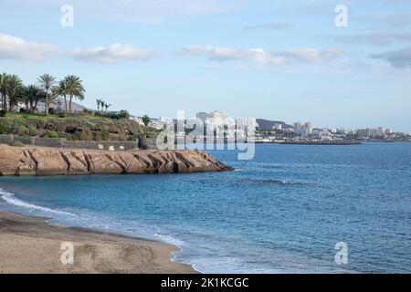Erhöhter Blick auf den beliebten Strand, das ruhige blaue Meer und die nahe gelegene Küste mit grünem Gras und üppigen tropischen Gärten, Playa del Duque, Costa Adeje Stockfoto