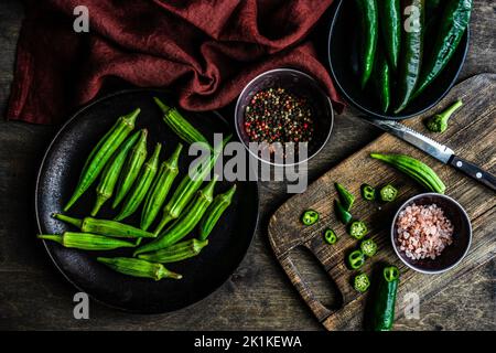 Ansicht von oben über die frische Okra, die mit grünen Chilis, Himalaya-Salz und gemischten Pfefferkörnern zubereitet wird Stockfoto