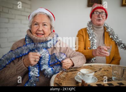 Glückliche ältere Freunde sitzen drinnen im Gemeindezentrum und feiern Weihnachten. Stockfoto