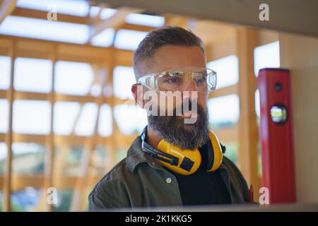 Zimmermann überprüft Holzbretter mit Wasserwaage, diy umweltfreundliche Häuser Konzept. Stockfoto