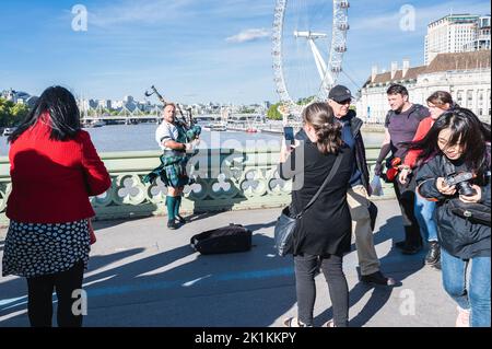 London, Großbritannien - 17 2022. September: Touristen, die Fotos von dem Mann im schottischen Kilt machen, der Dudelsäcke in der Nähe des Westminster Pier spielt, selektiver Fokus Stockfoto