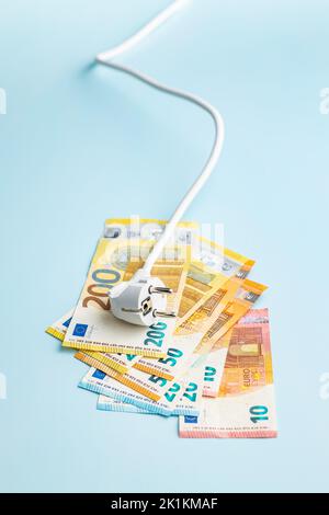 Elektrischer Stecker und Euro-Geld auf blauem Hintergrund. Konzept der steigenden Strompreise. Stockfoto