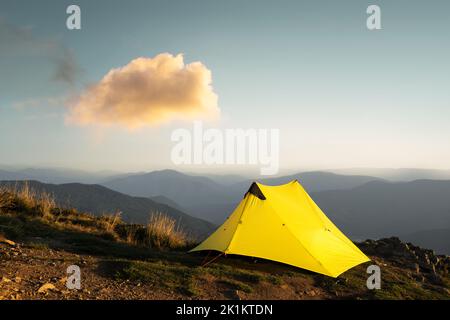 Gelbes Zelt vor der Kulisse einer unglaublichen Berglandschaft während des Morgensonnenaufgangs. Unglaubliches Hochland. Tourismuskonzept Stockfoto