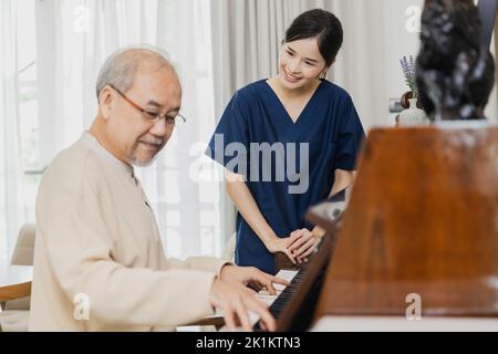 Asiatische Krankenschwester, Arzt Frau Assisting kümmern und zufrieden sein mit Senior asiatischen Patienten Mann Klavier spielen, um den Geist zu entspannen Stockfoto