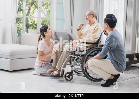 Glückliche Familie von Senioren mit schönen Tochter, ihr Mann und Enkel kümmern alten Mann auf Rollstuhl sitzen im Haus, positive Vater haben Stärke Stockfoto
