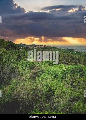 Eine vertikale Aufnahme des Sonnenlichts, das aus der Ferne durch dramatische Wolken über der Stadt blickt Stockfoto