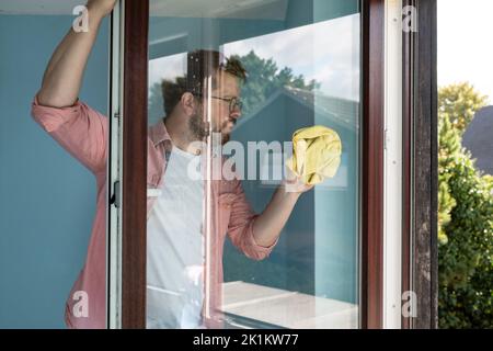 Fokussierter Mann öffnete den Fensterflügel und wäscht das Glas mit einem Lappen von Staub und Schmutz. Reinigung. Stockfoto