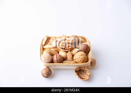 Verschiedene Nüsse in der Schale auf weißem Hintergrund: Walnüsse, Pekannüsse, Mandeln, Macadamia. Nüsse in einem Korb. Selektiver Fokus, Nahaufnahme. Für Text platzieren. Stockfoto