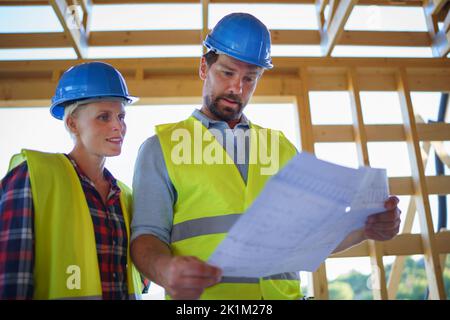 Bauingenieure oder Architekten mit Plänen zur Überprüfung der Öko-Baustelle des Holzrahmenhauses Stockfoto