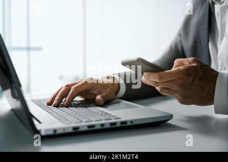 Geschäftsmann mit Smartphone und arbeiten auf Laptop-Computer im Büro. Business-Management und digitale Lösungen Konzept Stockfoto