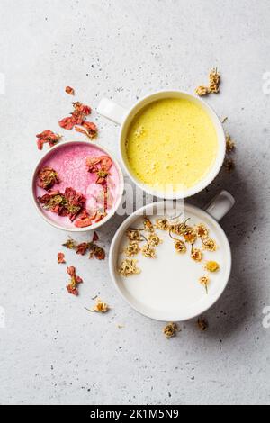 Verschiedene Arten von Mondmilch: Rosenblüte, goldener Kurkuma und Kamille in weißen Tassen, Draufsicht. Ayurveda-Getränk, gesunder Lebensstil, Heilmittel gegen Schlaflosigkeit Stockfoto