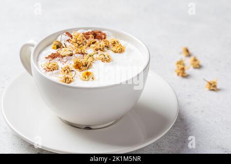 Kamillenmondmilch mit Zimt in einer weißen Tasse. Ayurveda-Getränk, Kamille-Latte-Tee. Stockfoto