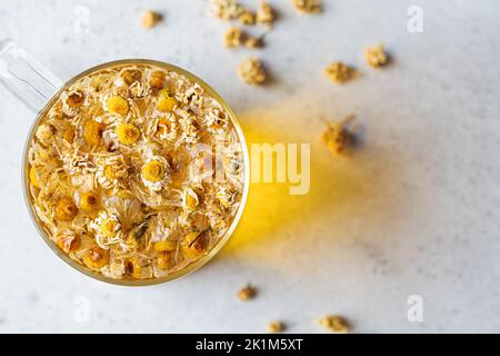 Kamillentee mit Blumen in einer Glasschale, Draufsicht. Gesundes Kräutergetränk, natürliches Antiseptikum und Unterstützung bei der Verdauung. Stockfoto