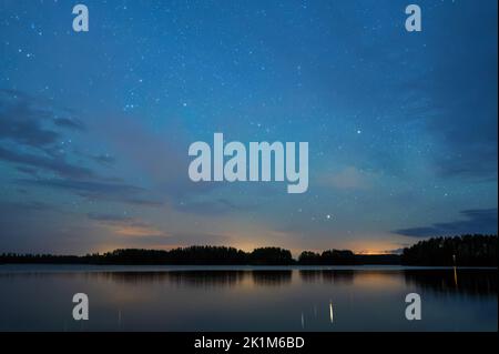 Nachtlandschaft unter Sternenhimmel, Sterne, die sich von der ruhigen Wasseroberfläche reflektieren, entfernter Donner am Horizont. Stockfoto