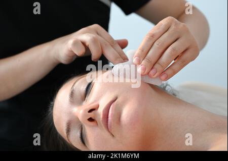 Junge Frau erhält Gesichtsmassage mit Gua Sha Werkzeug im Schönheitssalon. Nahaufnahme. Schönheitssalon Stockfoto