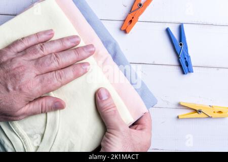 Eine Hand faltet die Kleidung und eine Pinzette Kleiderbügel auf dem Tisch Stockfoto