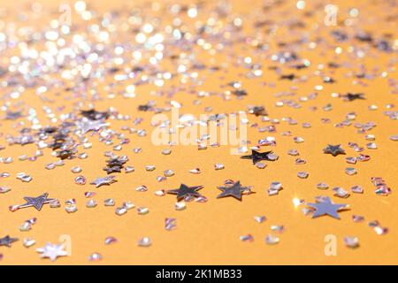Kleine silberne Sterne und Kristalle Konfetti auf einem gelben Hintergrund verstreut. Selektiver Fokus. Glänzende Textur. Stockfoto
