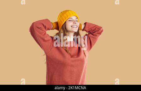 Entspannte Frau in Herbstkleidung legt die Hände hinter den Kopf, schließt die Augen, atmet Luft ein und lächelt Stockfoto