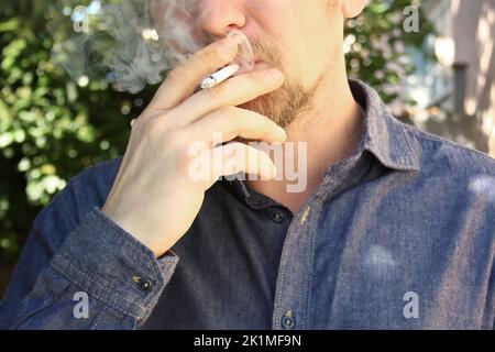 Rauchender Mann in Nahaufnahme in einem Hemd vor dem Hintergrund der Natur Stockfoto