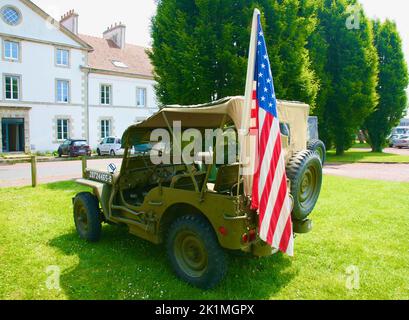 Ein alter amerikanischer Jeep, der die amerikanische Flagge im Hafen von Caretan in der Normandie, Frankreich, unterstützt Stockfoto