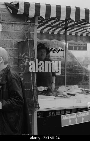 Die vertikale Graustufenansicht eines Fischverkäufers auf dem Straßenmarkt von HamburgAbstand halten Stockfoto