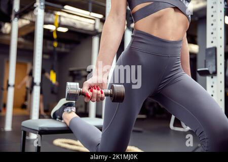 Attraktiv und fit Frau übt auf der Bank im Fitnessstudio und Hanteln. Horizontale Ansicht. Stockfoto