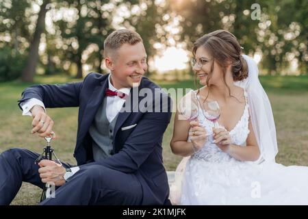 Junger Mann Bräutigam Eröffnung Flasche Wein, junge Frau Braut hält Gläser, Treffen Augen. Feier, Beziehung. Stockfoto