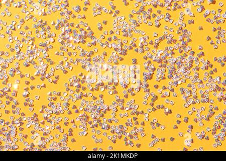 Winziges Konfetti aus silbernem Kristall auf gelbem Hintergrund. Leuchtende festliche Textur. Stockfoto