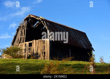 Holzscheune hat ein klaffendes Loch, wo der Dachboden sein sollte. Auf dem Blechdach fehlt Zinn. Verkommen Scheune liegt auf einem Hügel in Tennessee. Stockfoto