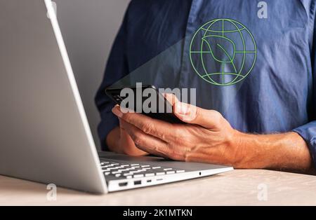 Das Konzept von „die“. Mann, der das Telefon hält, während er am Laptop arbeitet. Bewertung von Unternehmen mit ökologischen, sozialen und Governance-Kriterien. Anlagekonzept. Stockfoto