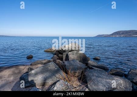 Felsbrocken als Teil eines Wellenbrechers in einem See. Bild vom See Vattern, Schweden. Blaues Wasser und Himmel im Hintergrund Stockfoto