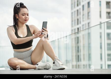 Sportlerin, die sich nach dem Training ausruhte und Nachrichten auf ihrem Telefon beantwortete Stockfoto