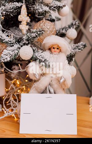 Grußkarte und Puppe stehen in der Nähe des Weihnachtsbaums Stockfoto