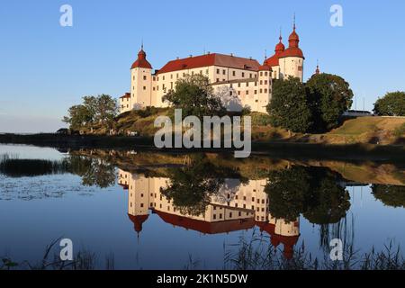 LIDKOPING, SCHWEDEN, 23. AUGUST 2022: Blick auf das Schloss Lacko (Läcko Slott) bei Sonnenuntergang, der sich in den ruhigen Gewässern des Vanernsees widerspiegelt. Die Burg ist ein beliebter tou Stockfoto