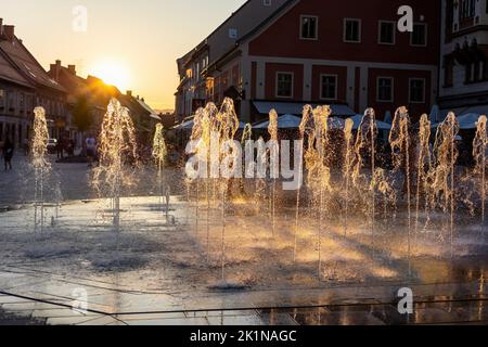 Wasserspritzung aus dem Brunnen in der Stadt Maribor, Slowenien, bei Sonnenuntergang. Stockfoto