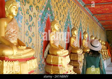 Weibliche Besucherin im Kloster mit einer großen Gruppe sitzender Buddha-Bilder im Tempel der Morgenröte oder im Wat Arun, Bangkok, Thailand Stockfoto