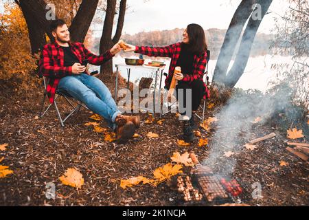Lächelndes, glückliches Paar, das am Feuer ausruhte und Essen kochte Stockfoto