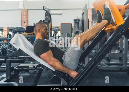 Mann, der während des Fitnesstrainings im Fitnessstudio auf Beindrücken trainiert, Full Shot Gym Lifestyle. Hochwertige Fotos Stockfoto