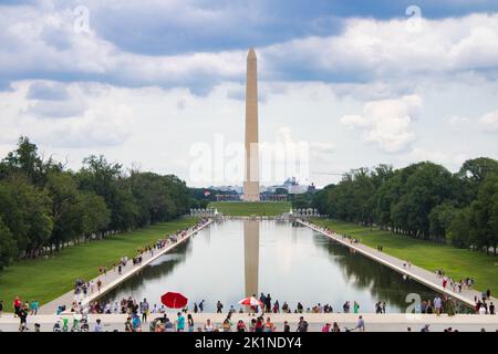 Blick auf das Washington Monument spiegelt sich an einem bewölkten Sommernachmittag in der National Mall im reflektierenden Pool wider. Menschenmassen können zu Fuß gesehen werden. Stockfoto