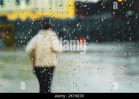 Abstrakter Hintergrundregen in der Nachtstadt, Silhouette einer jungen Frau hinter nassem Fenster durch Regentropfen auf Glas Stockfoto